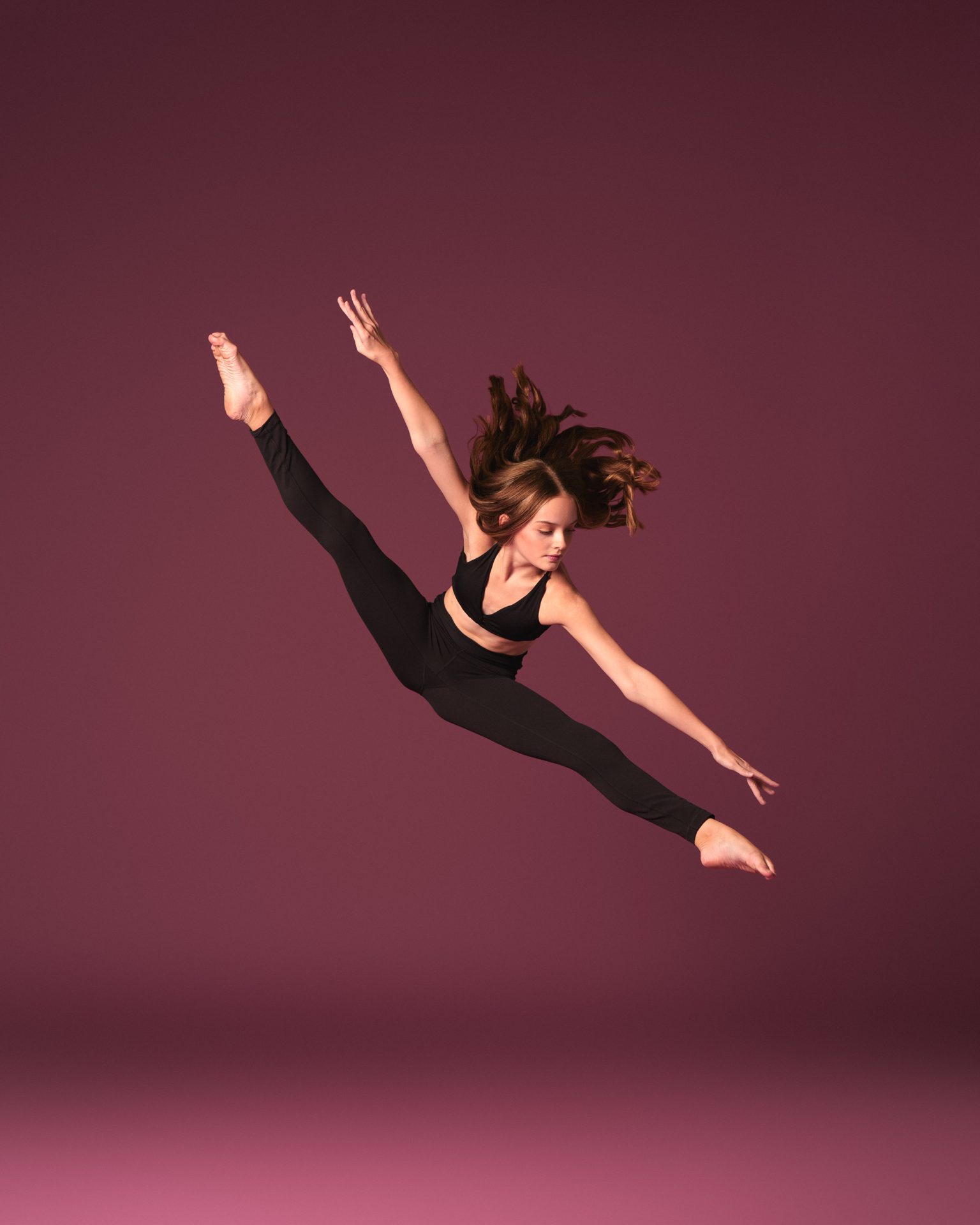 Company dancer in a grand jeté against a deep burgundy backdrop